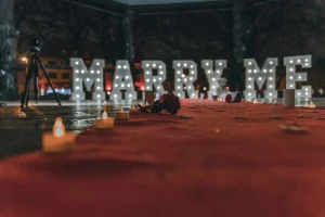 A romantic setup for a marriage proposal with lighted "Marry Me" sign and candles at night.